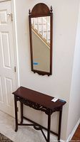 Wooden entry table with carved apron and matching rectangular mirror with arched top and finials mounted on wall.