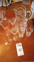 Full view of the etched glass pitcher and six assorted etched glasses on wooden surface.
