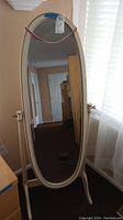 Full view of freestanding oval mirror with cream finish on wooden frame and stand.