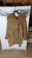 Brown suede jacket with shearling lining hung on hanger, showing front and general condition.
