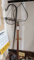 Wooden hose station post with brass water spigot and two black metal shepherd hooks with attached hanging baskets, shown standing against wall.