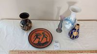 Lot overview showing five pottery items: black vase with gold design, decorative plate with Greek warriors, three other decorative vases.