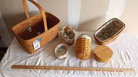 Full view of seven assorted Longaberger baskets in various sizes with lids and fabric/plastic inserts placed on white cloth.