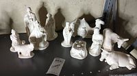All ceramic white figurines arranged showing full nativity set with animals and human figures.