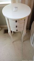 Front view of the round cream side table showing three drawers and curved legs