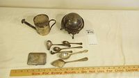 Overview of butter dish with lid, small pitcher or creamer with hinged lid, and six silver plated spoons laid out with measuring ruler