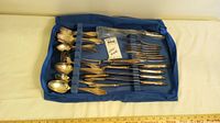 Full view of blue fabric storage case holding the silver plated silverware set arranged by type with forks, spoons, and serving utensils visible.