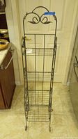 Front view of small silver metal bakers rack with 4 wire shelves and decorative scrolls