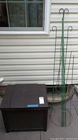 Photo of the brown Suncast small deck box and green wire lattice standing beside it on a patio by a siding wall.