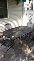 Wide shot showing the oval wrought iron outdoor table with mesh top and all four matching chairs around it.