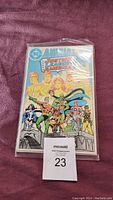 Photo of a Justice League of America Annual comic book in protective sleeve on purple fabric background with a lot number card.