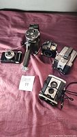 Four vintage cameras together on dark surface showing all items in the lot