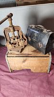 Overall view of rusty tool, black metal lunch box, and wooden box on surface