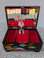Front open view of the 1950s black lacquered jewelry box showing red velvet interior divided into three compartments. Mirror with vertical sections installed on lid. Wind-up ballerina figurine visible in center.