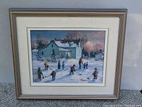Full view of the framed painting showing a blue house covered with snow, children playing hockey in the snow, and a dusk sky with trees. Artist signature visible at bottom right.