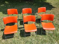 Six orange David Rowland 40/4 stacking chairs arranged outdoors on grass, showing front and side profiles.