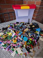 Photo showing a large pile of assorted LEGO pieces with a plastic carry case with red lid and yellow latch behind the pile.