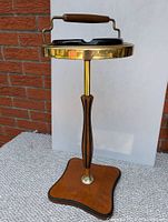 Full view of Mid-Century Modern ashtray stand showing wood base, brass top ring, black ceramic ashtray, and wooden handle.