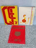 Three yearbooks laid on carpet floor showing front covers of three QECVI Centurion yearbooks 1969-1971.