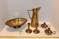 Full set showing brass candlestick holders, bowl, and jug arranged on a white backdrop with measuring tape for scale.