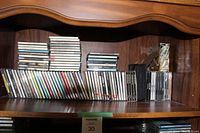 Shelf with approximately 30 music CDs in jewel cases and others, showing various spine labels.