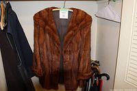 Full view of the brown fur coat hanging on a rack, showing the front with sleeves and collar details.