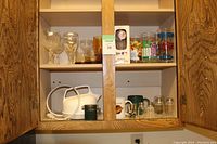 Overview of upper and middle shelves showing various drinking glasses, mugs, salt and pepper shakers, and white electric kettle with cord.