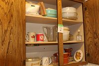 Photo of cabinet shelves showing various mugs, bowls, glass pitcher, and glass containers arranged on three shelves.