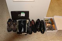 Five pairs of men's shoes all size 10 arranged on the floor next to two boxes, one labeled Clarks for the slippers and one containing shoe polishing items.