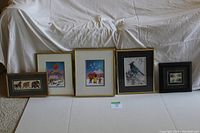 Overview of all five framed art pieces lined up on floor, showing a mix of Ted Harrison prints and other nature-themed art.