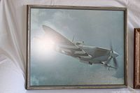 Print of Spitfire aircraft flying in a cloudy sky, framed, showing the artwork detail and size.