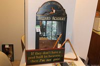 Photo showing vintage wooden mirror with Billiard Academy painted theme and wooden pool cue rack behind it, also includes a wooden sign with text about pool halls.