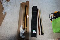 Four disassembled pool cues and black fabric soft sided cue case laid on carpet floor. Box containing some items visible.
