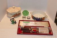Full lot displayed on white cloth showing mushroom casserole dish, green glass item, Toby jug, small glass containers, Villeroy & Boch casserole dish, and carving set in open case.