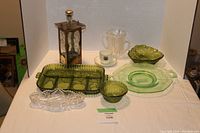 Photo showing the full lot including multiple green glassware items, a musical decanter, the coffee cup with saucer, and crystal dish on a white cloth.