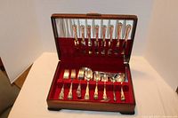 Full view of opened wooden case displaying vintage silver-plated cutlery pieces arranged in red velvet slots.