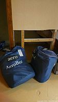 Two blue AeroBed carry bags placed on concrete floor in basement area, showing branding and general condition.