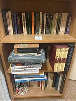 Full view of three shelves packed with various hardcover and paperback books on a wooden bookcase.