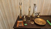 Photo showing all seven brass figurines and items arranged on a wood surface: four animal figurines, a pitcher, a plate, and a rectangular tray.