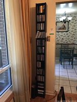 Tall black shelf against wall next to window, filled with multiple racks of CDs stored vertically and horizontally.