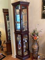 Full view of the tall corner display cabinet with glass shelves filled with figurines, placed against a wall corner.