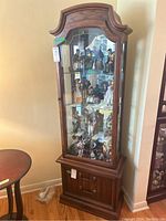 Front view showing the wood veneer display cabinet with glass front, three glass shelves filled with various figurines, mirror back, and two lower wood drawers with metal pulls.