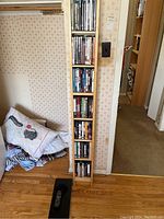 Wooden vertical shelving unit filled with DVDs and BluRay discs visible with some movie titles.