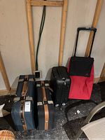 Full view of all four luggage items showing two soft-sided suitcases with leather accents, black hard-sided suitcase, and red wheeled canvas shopper
