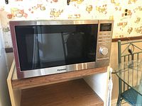 Microwave oven front and side view on wooden shelf, showing stainless steel frame and control panel.