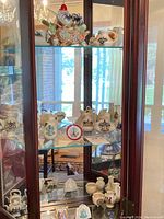 Overview of three glass shelves with multiple miniature ceramic jugs, pitchers, and figurines.