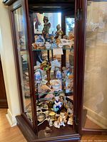 Overall view of three glass shelves filled with various miniature figurines and collectibles inside a wooden display cabinet.