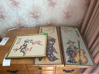 Four framed textile artworks displayed on wood dresser, featuring Asian themed needlepoint and silk embroidery with gold bamboo style frames.