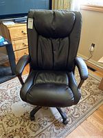 Front view of black faux leather office chair with padded backrest, seat, and armrests, on caster wheels.