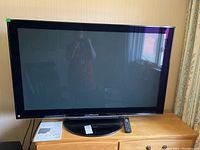 Front view of the Panasonic 50 inch plasma HDTV on stand with remote and manual on the stand surface.